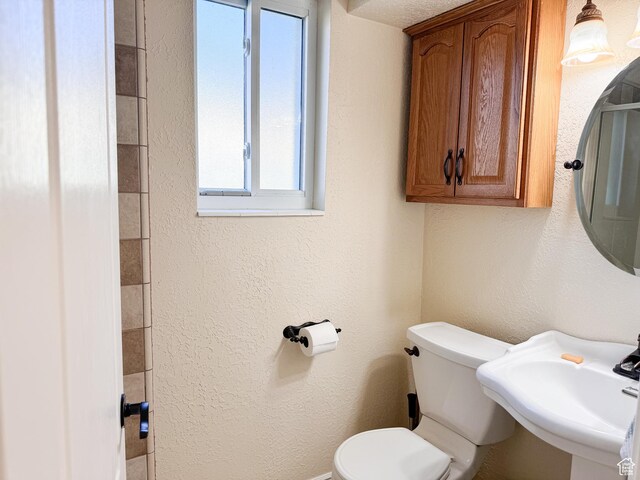 bathroom with toilet, a textured wall, and a sink