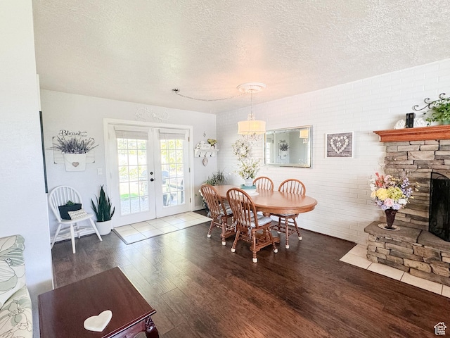 dining area featuring a stone fireplace, wood finished floors, french doors, and a textured ceiling