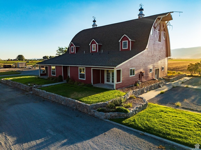 view of front of house with a gambrel roof, french doors, a barn, a front lawn, and a shingled roof