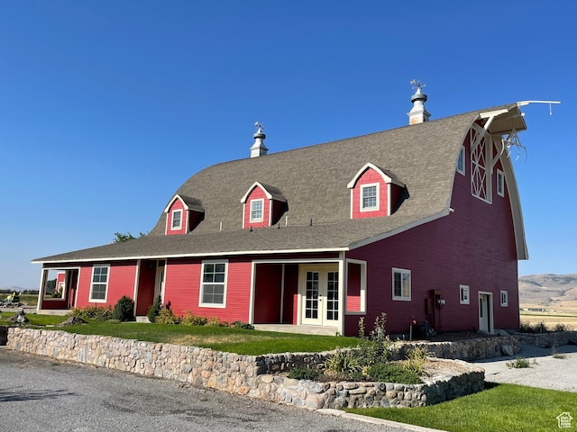 view of front of house with a shingled roof, french doors, a barn, and a front yard