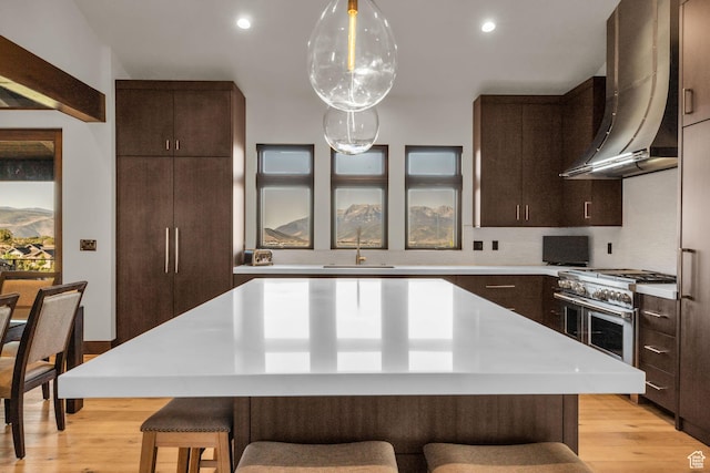 kitchen featuring a kitchen island, wall chimney range hood, a kitchen breakfast bar, and dark brown cabinetry