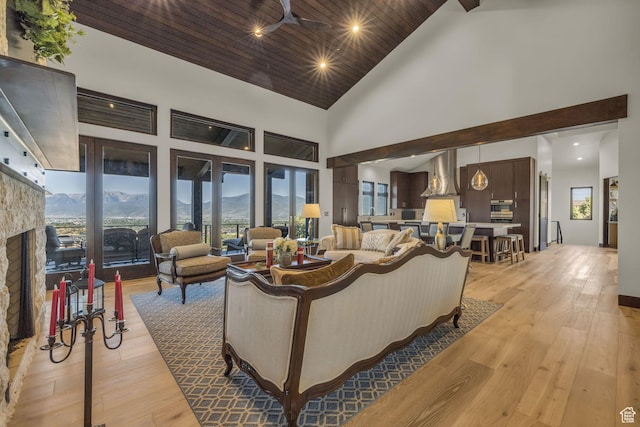 living area featuring high vaulted ceiling, a ceiling fan, a stone fireplace, light wood finished floors, and wooden ceiling
