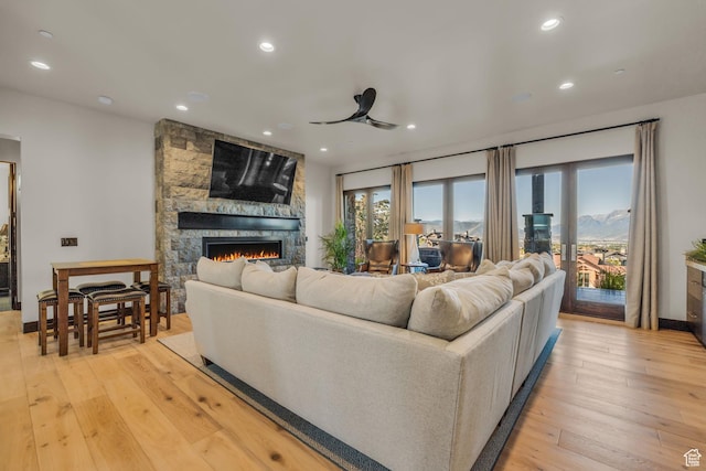 living area featuring light wood-type flooring, ceiling fan, a fireplace, baseboards, and recessed lighting