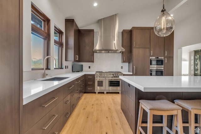 kitchen with a kitchen breakfast bar, stainless steel appliances, light countertops, a sink, and wall chimney exhaust hood