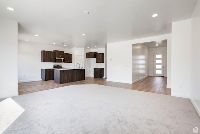 unfurnished living room featuring baseboards, a sink, light wood finished floors, and recessed lighting