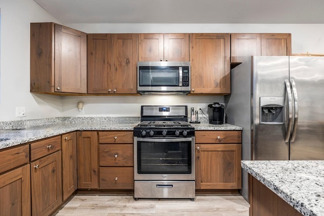 67 E 500 S Unit B102, Heber City, UT 84032 - kitchen with appliances with stainless steel finishes, brown cabinets, light stone countertops, and light wood-type flooring