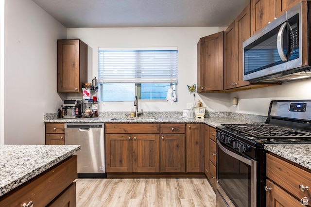 67 E 500 S Unit B102, Heber City, UT 84032 - kitchen featuring appliances with stainless steel finishes, a sink, light wood-style floors, light stone countertops, and brown cabinets
