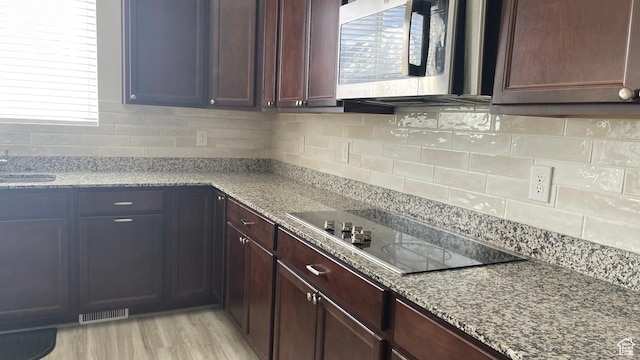 kitchen featuring black electric cooktop, visible vents, stainless steel microwave, and light stone counters