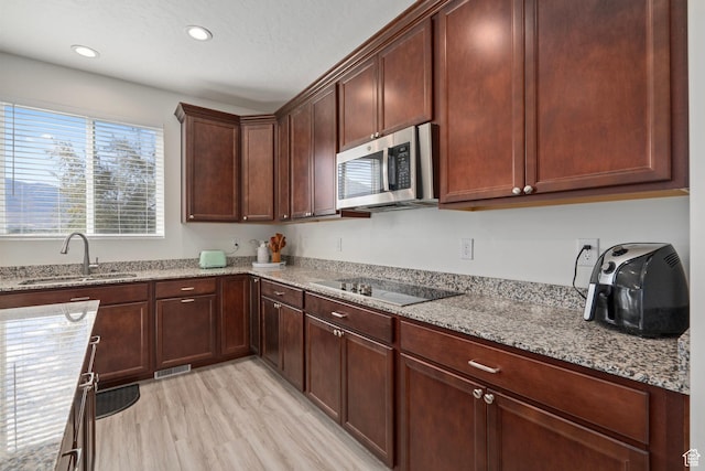 kitchen featuring a sink, stainless steel microwave, electric cooktop, visible vents, and light stone counters