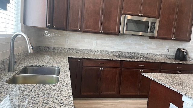 kitchen featuring black electric cooktop, light stone counters, backsplash, a sink, and stainless steel microwave