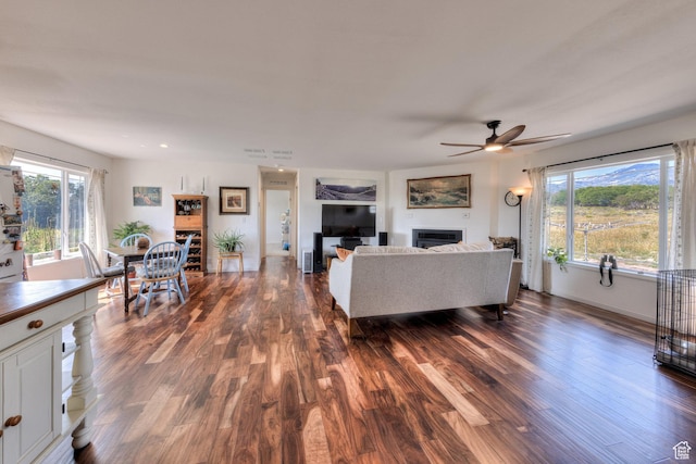 living area with dark wood-type flooring, baseboards, a ceiling fan, and a fireplace