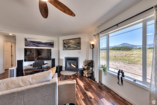 living area featuring a glass covered fireplace, dark wood-style flooring, baseboards, visible vents, and ceiling fan
