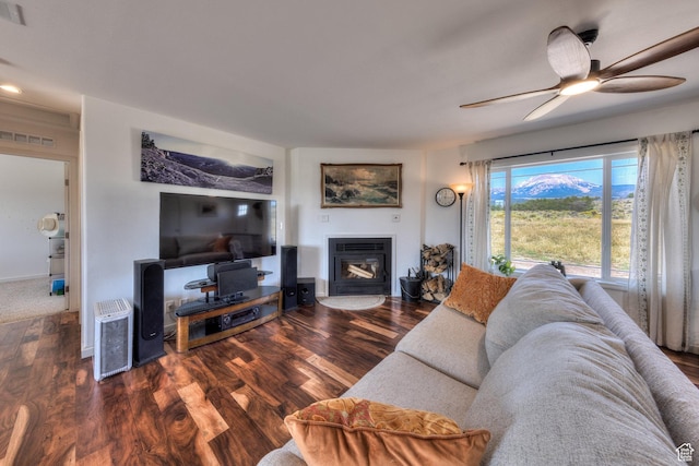 living area featuring a glass covered fireplace, visible vents, a ceiling fan, and wood finished floors