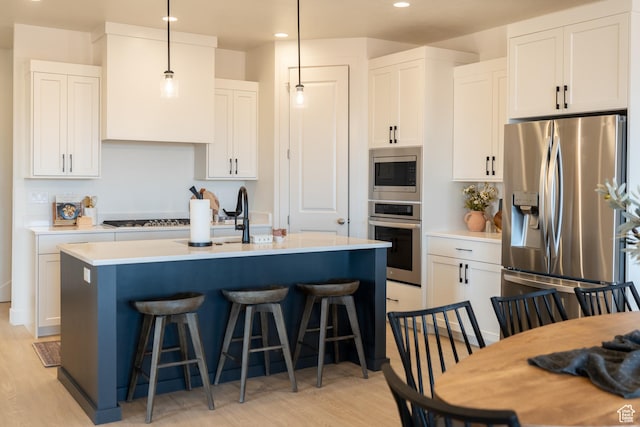 5394 S Aquamarine Ln, St George, UT 84790 - kitchen with white cabinets, a center island with sink, hanging light fixtures, light wood-type flooring, and stainless steel appliances