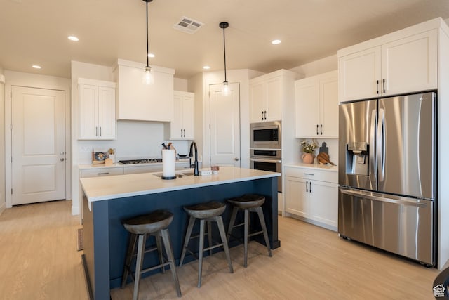 5394 S Aquamarine Ln, St George, UT 84790 - kitchen featuring backsplash, white cabinets, a center island with sink, light hardwood / wood-style flooring, and appliances with stainless steel finishes
