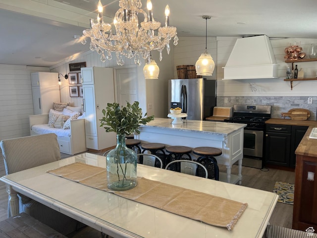 dining area featuring light wood-style floors, a chandelier, wood walls, and vaulted ceiling