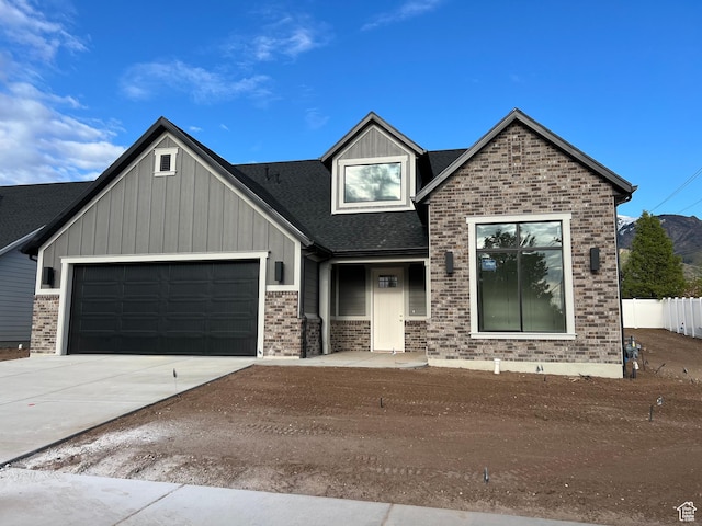 view of front facade featuring a garage, brick siding, a shingled roof, board and batten siding, and driveway