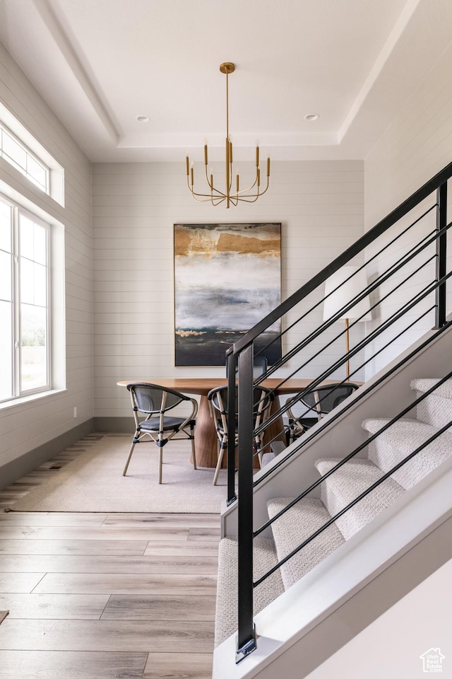 staircase with baseboards, a tray ceiling, wood finished floors, and a chandelier