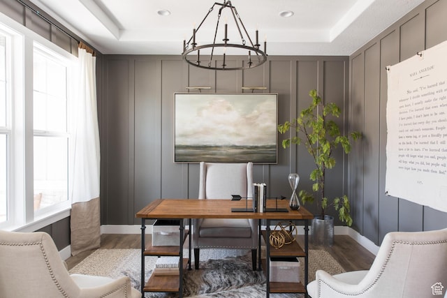 office area featuring a decorative wall, a tray ceiling, a chandelier, and wood finished floors