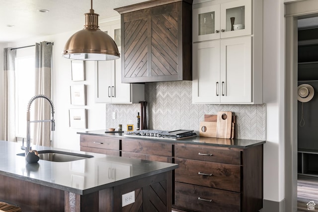 kitchen with stainless steel gas stovetop, custom exhaust hood, dark countertops, tasteful backsplash, and a sink