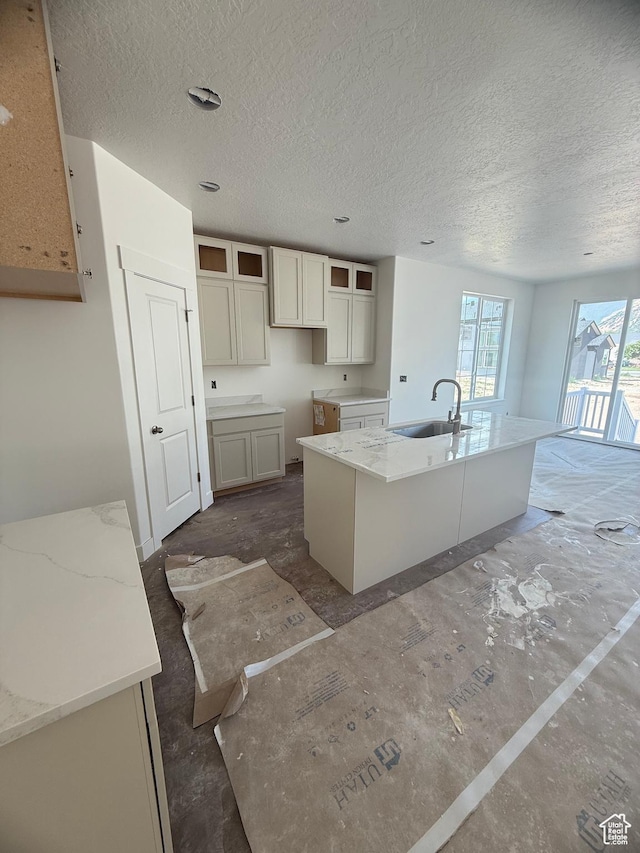 314 N 1040 E Unit 24, Salem, UT 84653 - kitchen featuring a sink, a center island with sink, a textured ceiling, light stone countertops, and glass insert cabinets