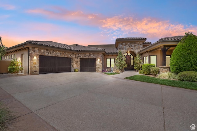 view of front of property featuring a garage, stone siding, a tiled roof, concrete driveway, and stucco siding