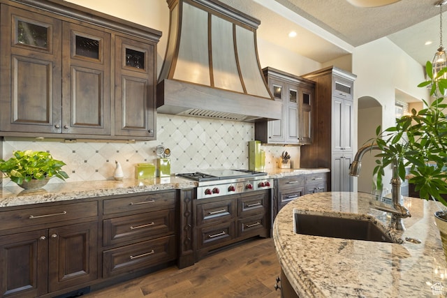 2596 E Flint St, St George, UT 84790 - kitchen with stainless steel gas cooktop, custom exhaust hood, glass insert cabinets, dark wood-style flooring, and a sink