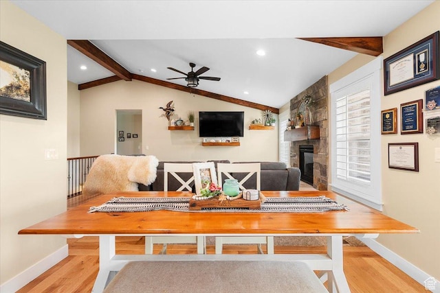 dining space featuring lofted ceiling with beams, wood finished floors, a large fireplace, baseboards, and ceiling fan