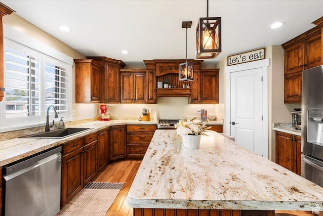 kitchen with a sink, a center island, hanging light fixtures, light wood-style flooring, and stainless steel appliances