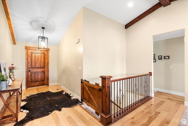 corridor with hardwood / wood-style floors, an upstairs landing, beam ceiling, and baseboards