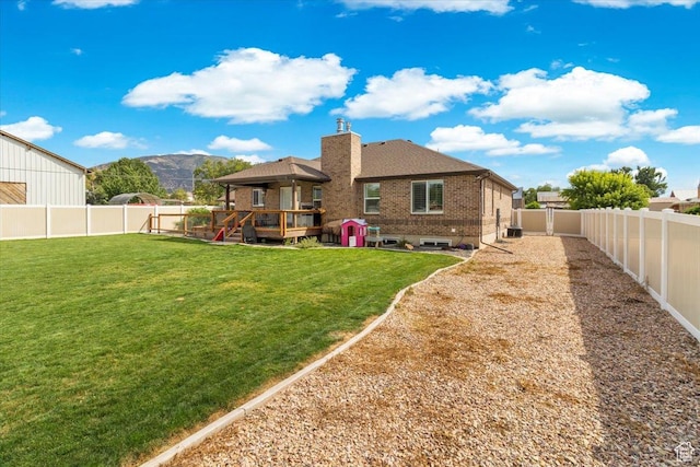 back of house with a fenced backyard, a mountain view, brick siding, and a yard