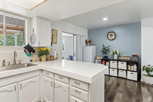 kitchen with dark wood-type flooring, light countertops, a peninsula, white cabinetry, and a sink