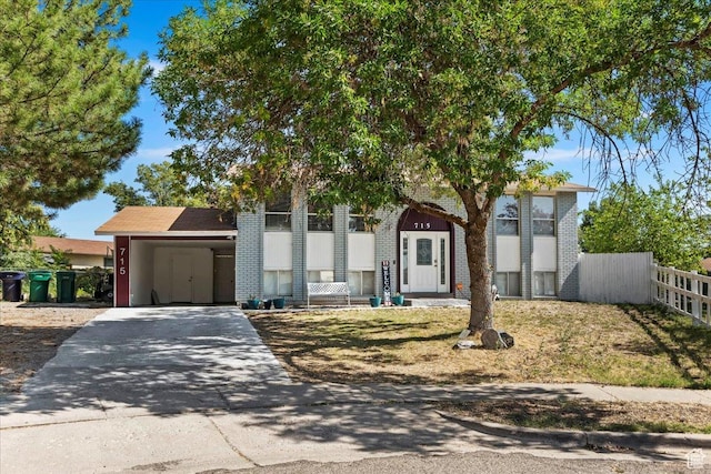 bi-level home with brick siding, a carport, driveway, and fence