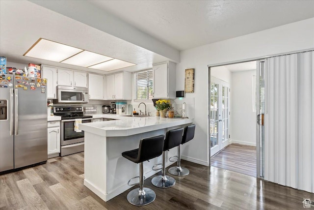 kitchen featuring a kitchen bar, a sink, appliances with stainless steel finishes, a peninsula, and light countertops
