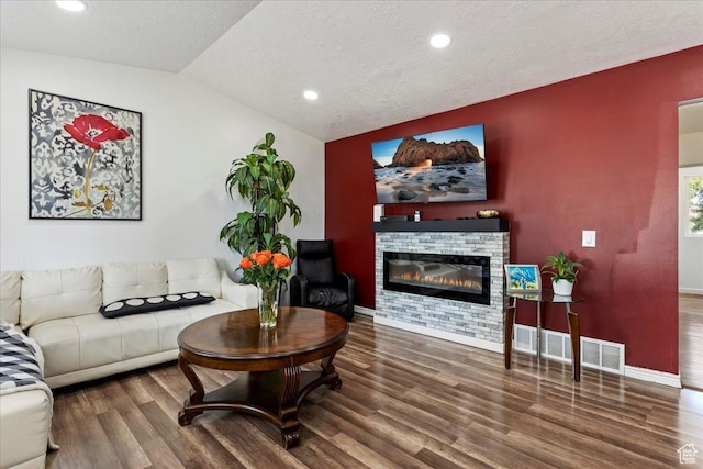 living area featuring visible vents, vaulted ceiling, wood finished floors, a glass covered fireplace, and a textured ceiling