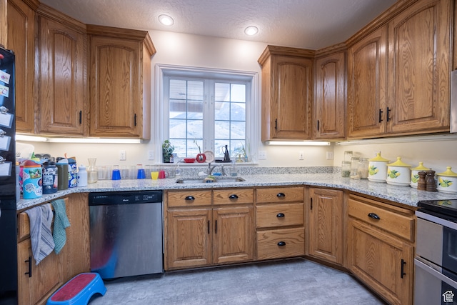 kitchen with a textured ceiling, light stone counters, stainless steel appliances, and sink