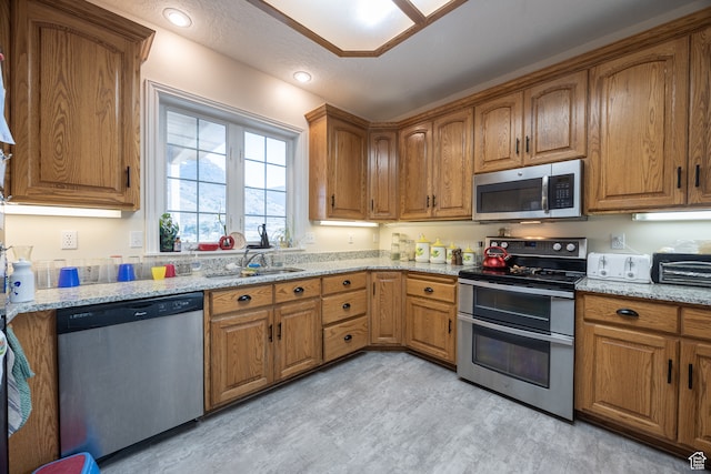 kitchen with a textured ceiling, stainless steel appliances, sink, and light stone countertops