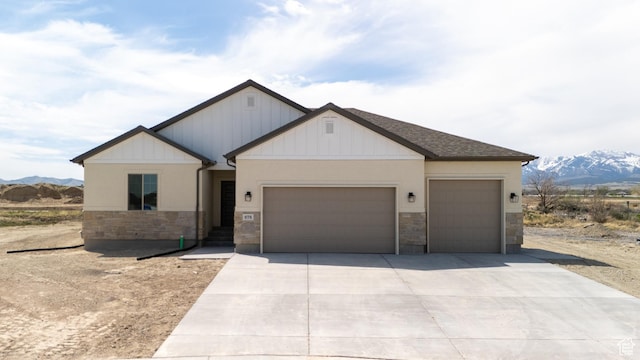 view of front of home with a shingled roof, concrete driveway, an attached garage, stone siding, and a mountain view