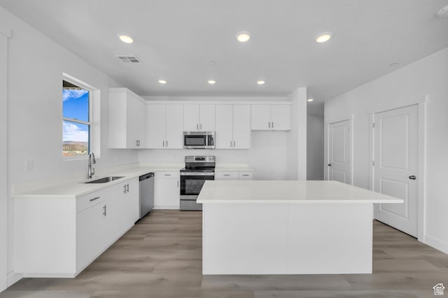 kitchen featuring visible vents, a kitchen island, appliances with stainless steel finishes, white cabinets, and a sink