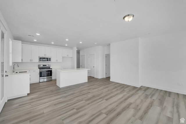 kitchen with light wood-style flooring, a sink, appliances with stainless steel finishes, white cabinets, and light countertops