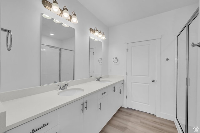 bathroom featuring double vanity, a shower stall, wood finished floors, and a sink