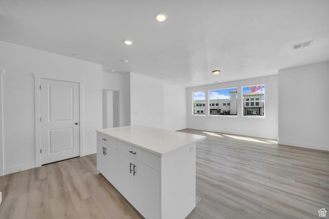 kitchen with white cabinetry, light wood-style flooring, visible vents, and a center island