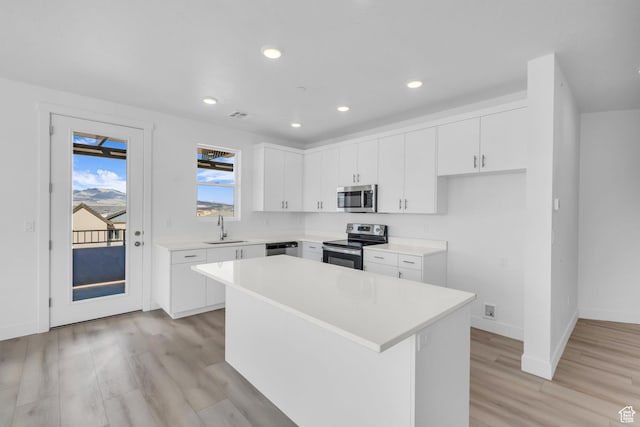 kitchen with a center island, light countertops, light wood-style floors, stainless steel appliances, and a sink