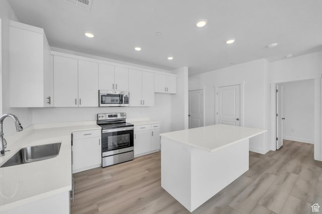 kitchen with light wood finished floors, a sink, stainless steel appliances, light countertops, and white cabinets