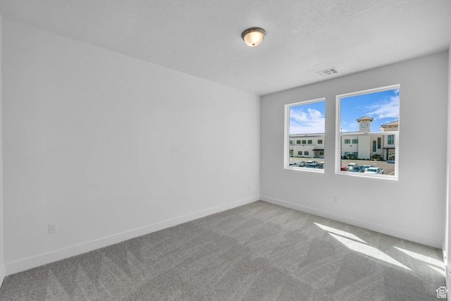 carpeted spare room featuring visible vents, baseboards, and a textured ceiling