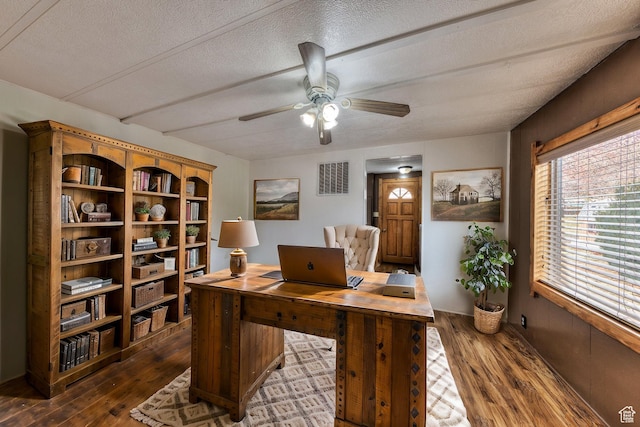 office featuring a textured ceiling, ceiling fan, visible vents, and dark wood-style flooring