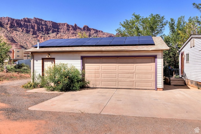 garage featuring a mountain view, solar panels, and driveway