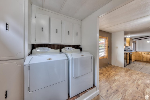clothes washing area with light wood finished floors, washer and clothes dryer, a sink, and cabinet space