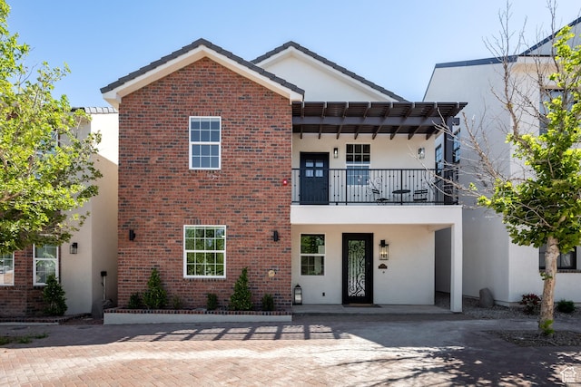 view of front of property featuring brick siding, a balcony, and stucco siding