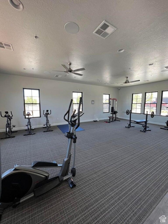 workout area featuring a textured ceiling, visible vents, a ceiling fan, and baseboards